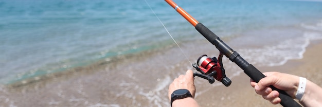 Homem gira a linha no carretel da vara de pescar no mar. Conceito de regras de pesca recreativa