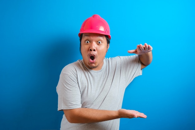 Homem gordo asiático usando um capacete apresenta algo na mão enquanto está voltado para o lado. o homem mostrou uma expressão de alegria e surpresa