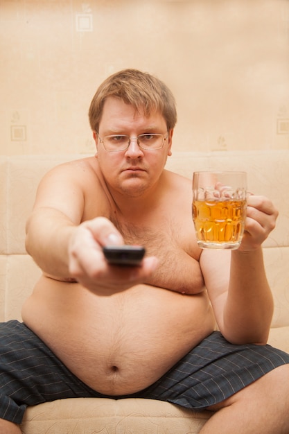 Homem gordo com barriga de cerveja na frente da tv comendo pipoca e bebendo cerveja