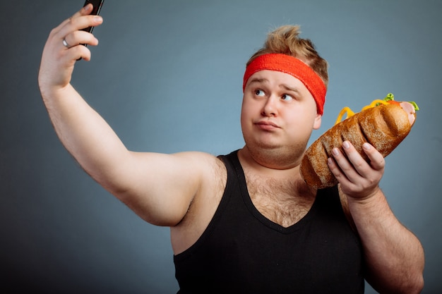 Foto homem gordo com sanduíche na mão faz selfie