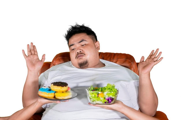 Homem gordo duvidoso escolhe salada ou donuts no estúdio