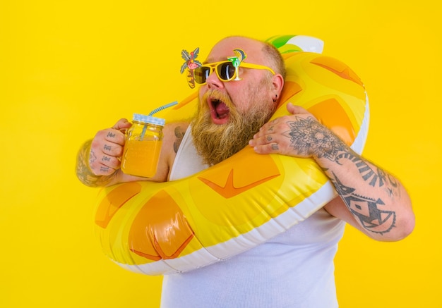 Foto homem gordo e faminto com peruca na cabeça está pronto para nadar com um salva-vidas de donut