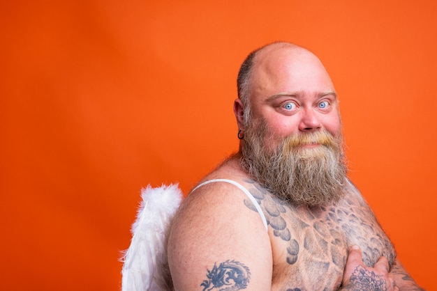 Homem gordo e feliz com tatuagens de barba e asas agindo como um anjo