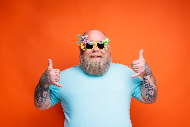 Homem gordo e feliz com tatuagens de barba e óculos de sol está pronto para o verão