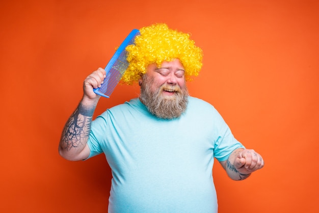 Homem gordo e feliz com tatuagens de barba e óculos de sol se penteando com um pente gigante