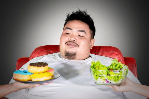 Homem gordo escolhendo donuts enquanto senta no sofá