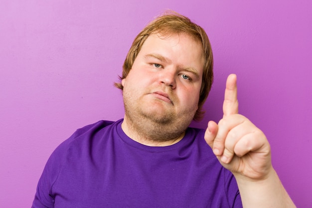 Homem gordo jovem ruiva autêntica, mostrando o número um com o dedo.