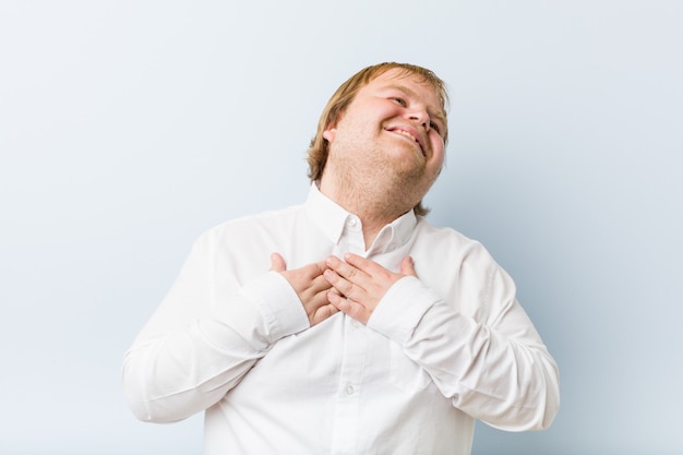 Homem gordo jovem ruiva autêntica rindo mantendo as mãos no coração, de felicidade.