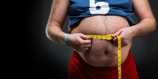 Homem gordo medindo sua grande barriga sobre cinza