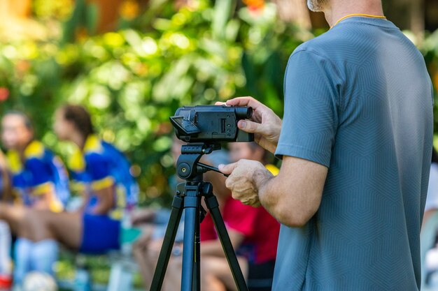 Homem gravando jogo de futebol com sua câmera de vídeo em um tripé em um campo ao ar livre