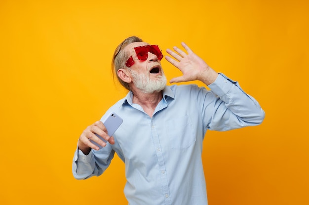 Homem grisalho sênior em óculos vermelhos na moda com um fundo isolado de telefone