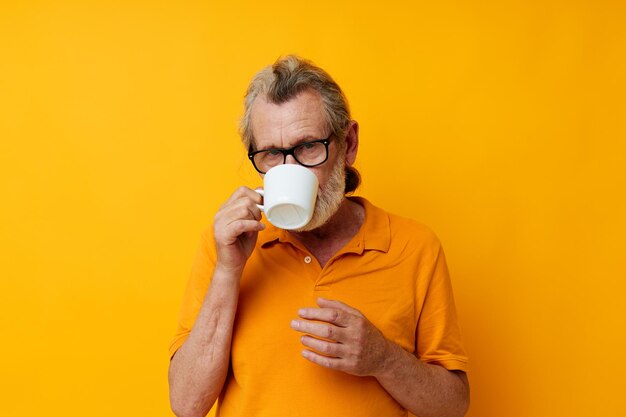 Homem grisalho sênior em uma caneca branca de camiseta amarela isolada de fundo