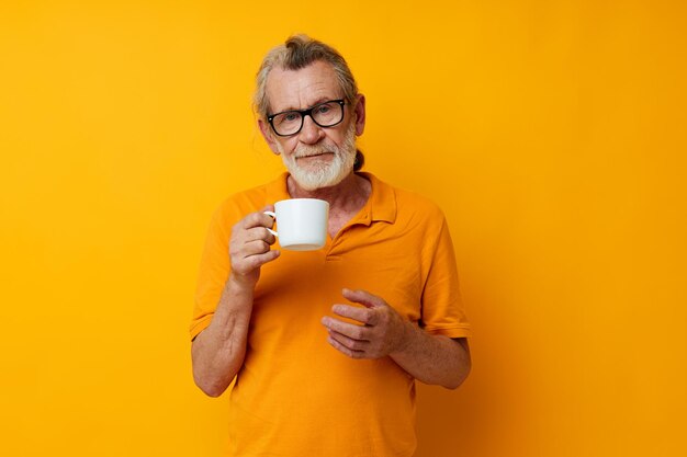 Homem grisalho sênior em uma caneca branca de camiseta amarela isolada de fundo