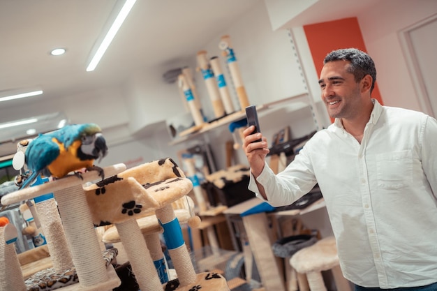 Homem grisalho sorrindo enquanto tira foto de papagaio