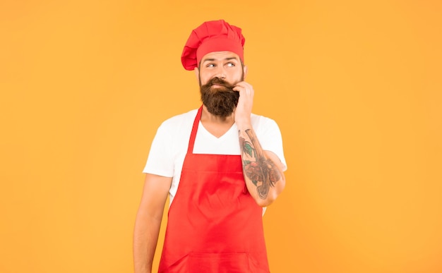 Foto homem hesitante de toque vermelho e avental a acariciar o queixo com fundo amarelo