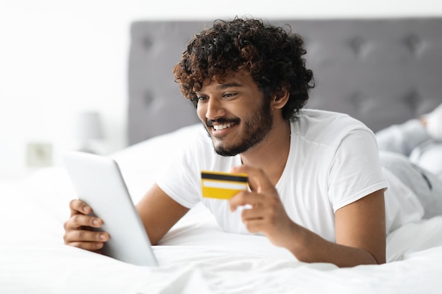 Homem hindu sorridente usando tablet digital e cartão de crédito