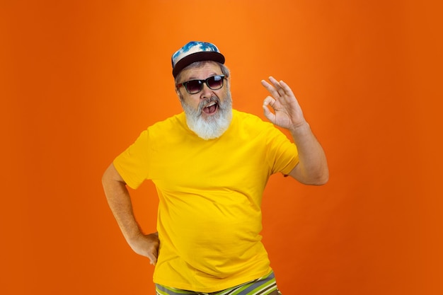 Homem hippie sênior usando dispositivos, gadgets em fundo laranja