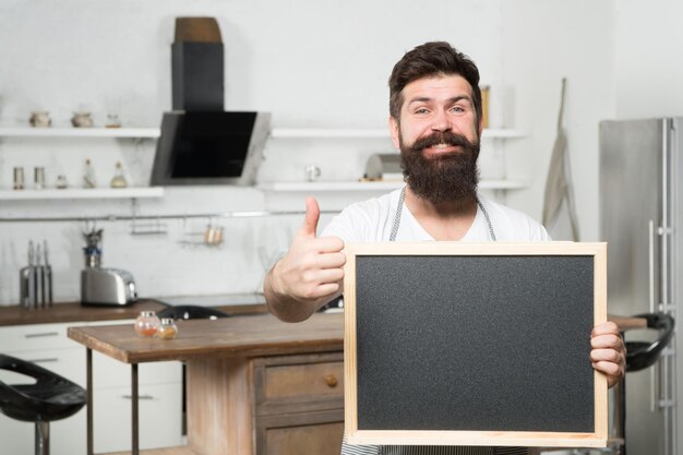 Homem hipster barbudo segura lousa para espaço de cópia e mostra o polegar para cima promoção