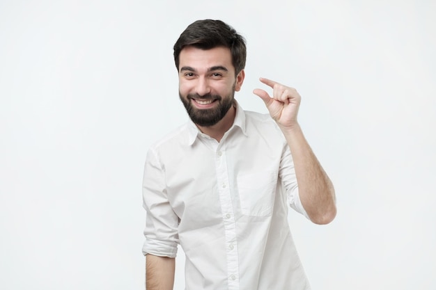 Homem hispânico bonito mostrando algo pequeno com as mãos enquanto gesticula e sorri amplamente