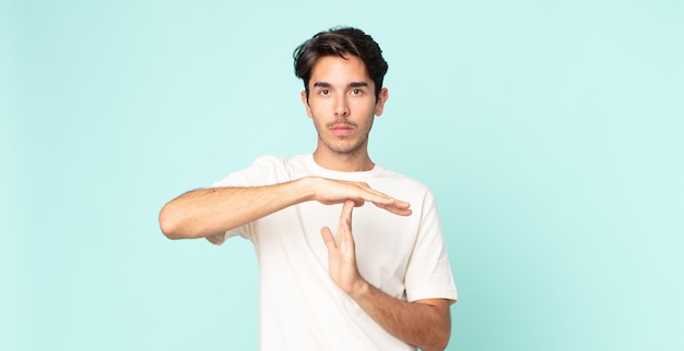 Homem hispânico bonito parecendo sério, severo, zangado e descontente, fazendo sinal de tempo limite