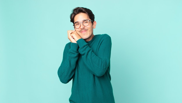 Homem hispânico bonito se apaixonando e parecendo fofo, adorável e feliz, sorrindo romanticamente com as mãos ao lado do rosto