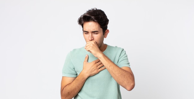 Homem hispânico bonito se sentindo mal, com dor de garganta e sintomas de gripe, tosse com a boca coberta