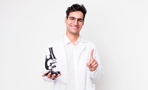 Homem hispânico bonito sorrindo com orgulho e confiança fazendo cientista número um com conceito de microscópio