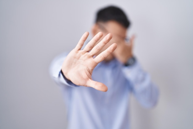 Homem hispânico bonito vestindo roupas de negócios e óculos cobrindo os olhos com as mãos e fazendo gesto de parada com expressão triste e de medo. conceito envergonhado e negativo.