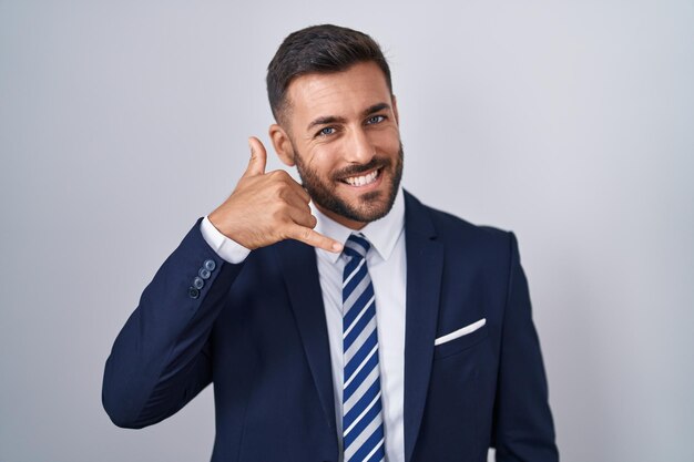 Homem hispânico bonito vestindo terno e gravata sorrindo fazendo gesto de telefone com a mão e os dedos como falar ao telefone. comunicar conceitos.