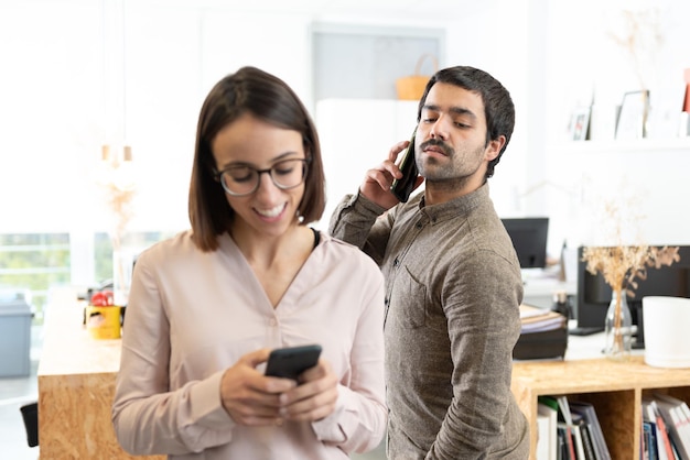 Homem hispânico com bigode espionando o telefone de sua colega de trabalho enquanto ela está conversando.