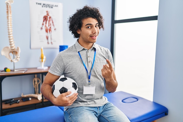 Foto homem hispânico com cabelo encaracolado trabalhando como fisioterapeuta de futebol acenando venha aqui gesto com a mão convidando feliz e sorridente