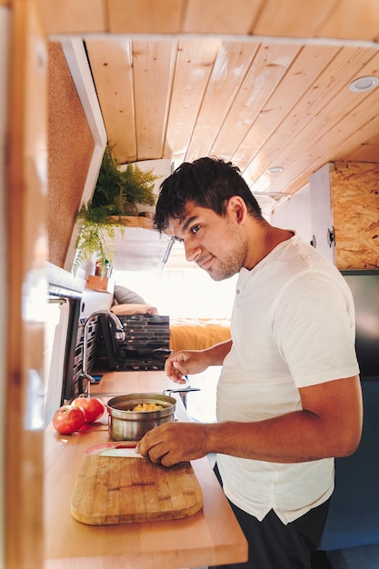 Homem hispânico cozinhando comida para refeição na cozinha de sua van de campista Van viagem de férias e aventura de verão ao ar livre Conceito de estilo de vida nômade