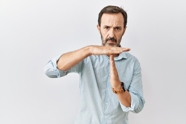 Homem hispânico de meia-idade com barba em pé sobre fundo isolado fazendo gesto de tempo com as mãos, rosto sério e frustrado