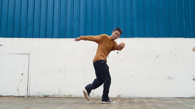 Homem hispânico estende os braços e dança dança de rua em frente à parede Endeavour