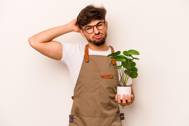 Homem hispânico jovem jardineiro segurando uma planta isolada no fundo branco, chocada, ela se lembrou de uma reunião importante