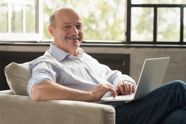 Homem hispânico sênior na sala de estar com laptop sorrindo