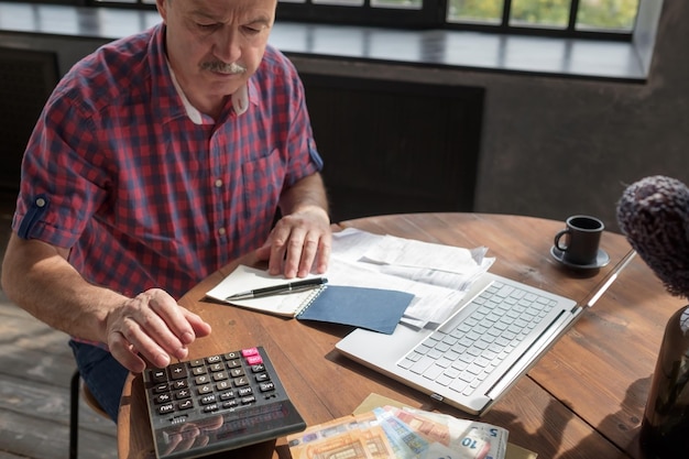 Homem hispânico sênior ocupado fazendo cálculos contando dinheiro e contas em casa