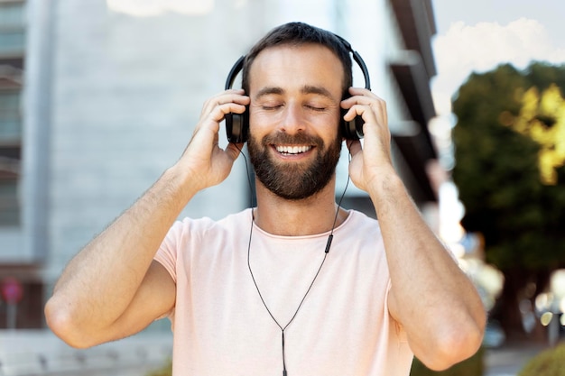 Homem hispânico sorridente ouvindo música com os olhos fechados em pé na rua