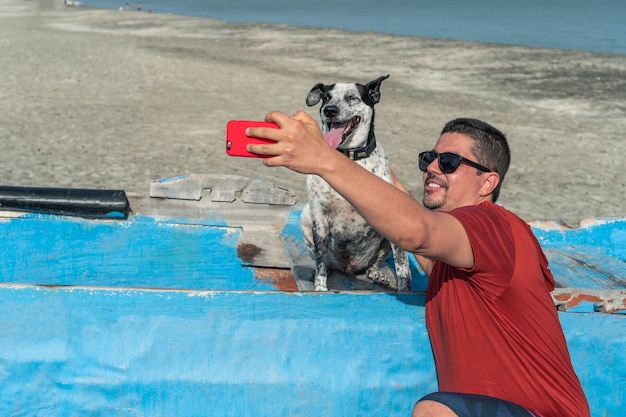 Homem hispânico tirando uma selfie com seu cachorro na praia no verão