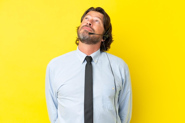 Homem holandês de telemarketing trabalhando com um fone de ouvido isolado em fundo amarelo e olhando para cima