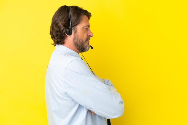 Homem holandês de telemarketing trabalhando com um fone de ouvido isolado em fundo amarelo em posição lateral