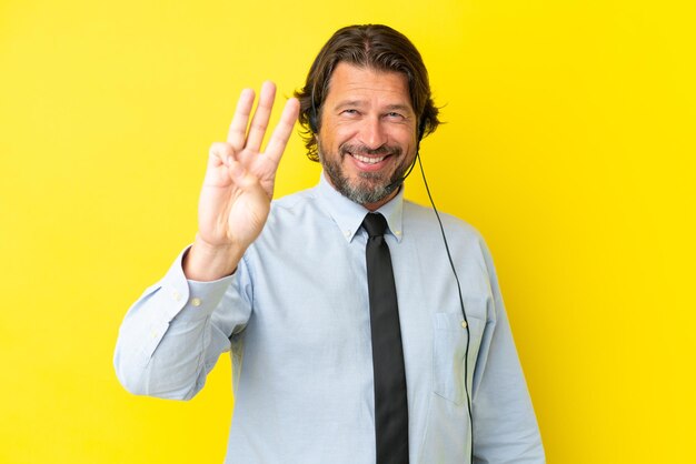 Homem holandês de telemarketing trabalhando com um fone de ouvido isolado em fundo amarelo feliz e contando três com os dedos