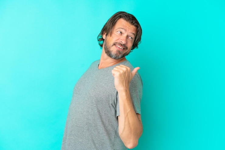 Foto homem holandês sênior isolado em fundo azul, apontando para o lado para apresentar um produto