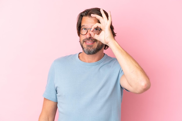 Homem holandês sênior isolado em fundo rosa com óculos e uma expressão feliz