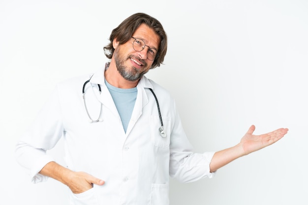 Foto homem holandês sênior isolado no fundo branco, usando uma bata de médico e apresentando algo