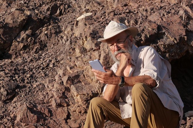 Homem idoso a usar telemóvel no deserto