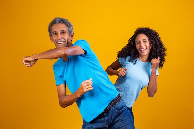 Homem idoso afro com sua filha dançando.