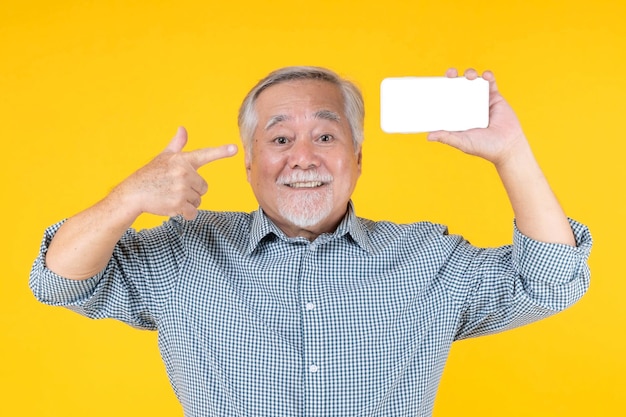 Homem idoso asiático se sente feliz e com boa saúde rosto surpreso animado mostrando telefone inteligente com tela em branco tela branca isolada em fundo amarelo mock up image