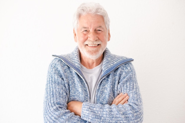 Homem idoso barbudo feliz em roupas casuais sorrindo e olhando para a câmera em pé com os braços cruzados no fundo branco