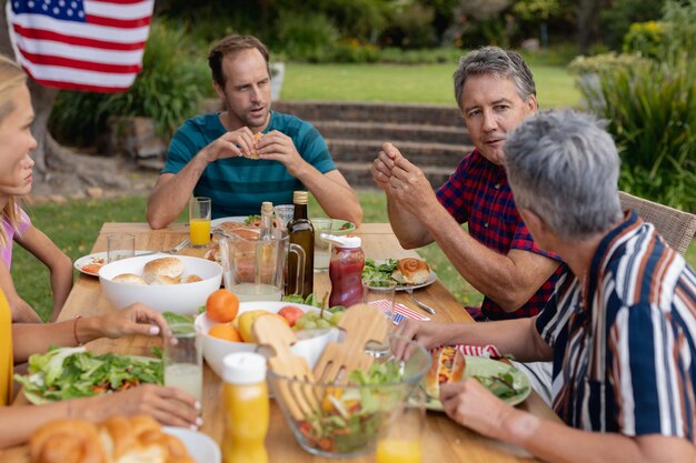 Foto homem idoso caucasiano sentado à mesa falando com a família tendo uma refeição de celebração no jardim